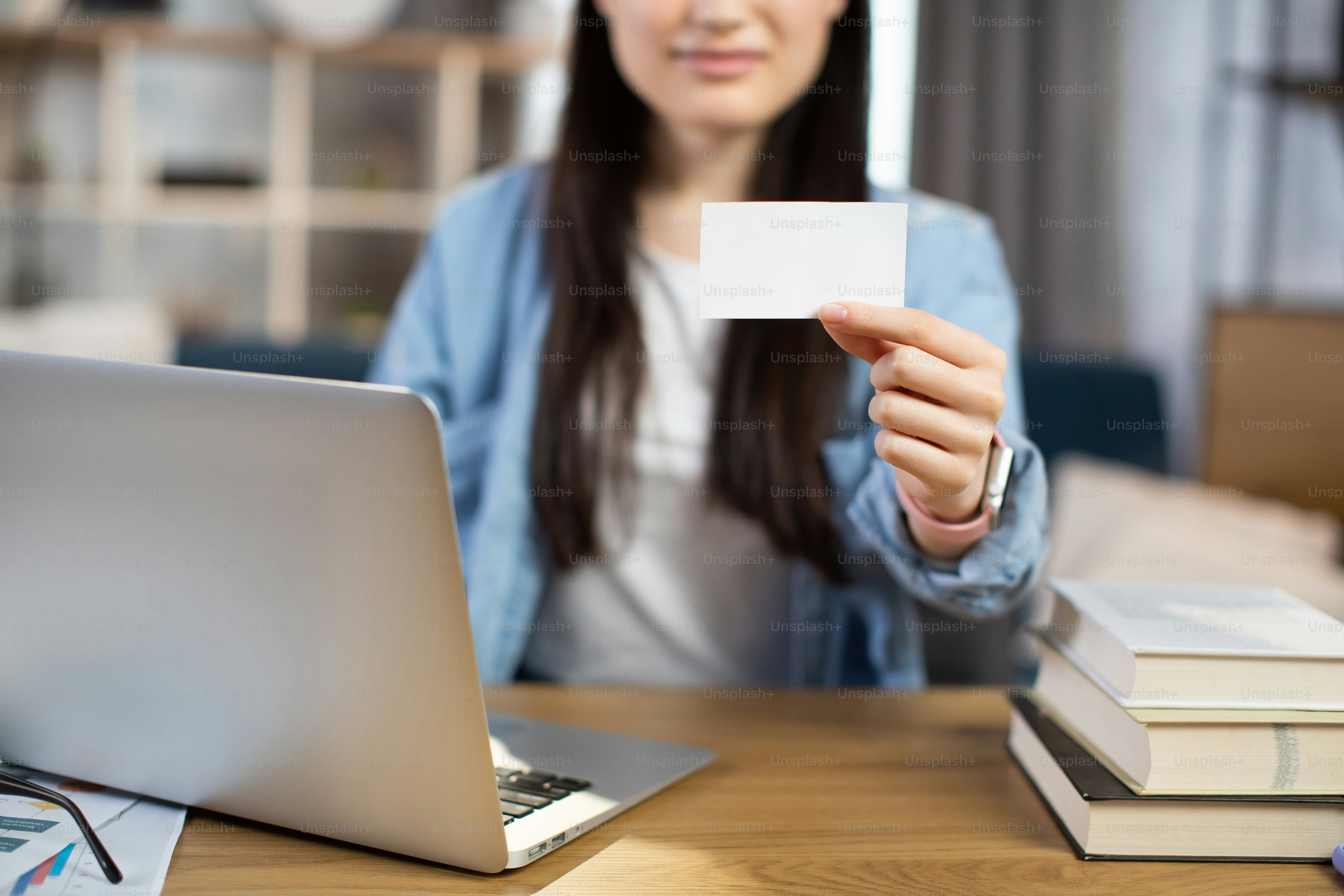 Close up of female manager or office worker sitting at table with modern laptop and showing on camera white empty business card. Concept of marketing and occupation. Empty space for text